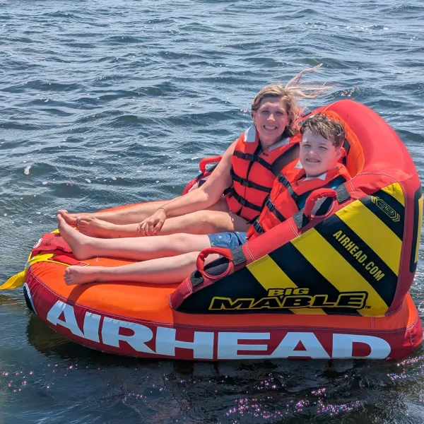 Two people smiling on an inflatable raft on the water, wearing orange life vests.