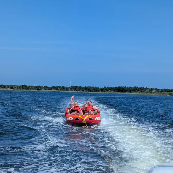 Two people tubing on a red inflatable, being pulled by a boat on a lake.