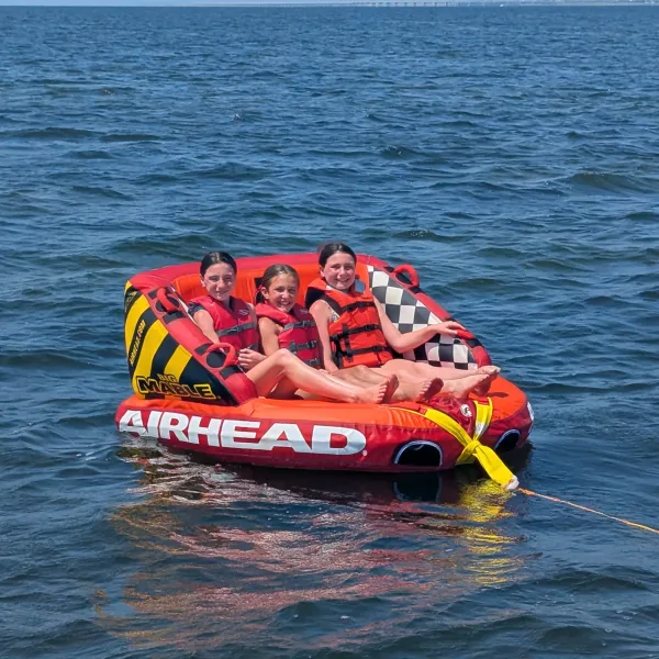 Three people on a red inflatable raft on a lake, wearing life jackets.