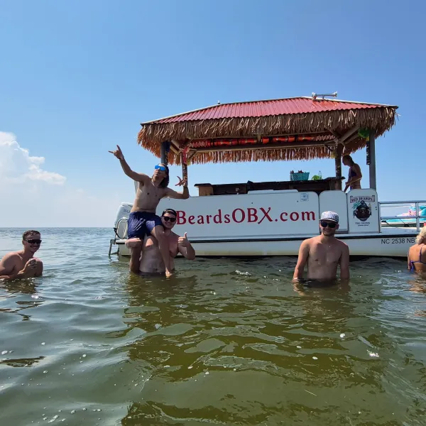 Group of people enjoying water near a tiki bar boat in sunny weather.
