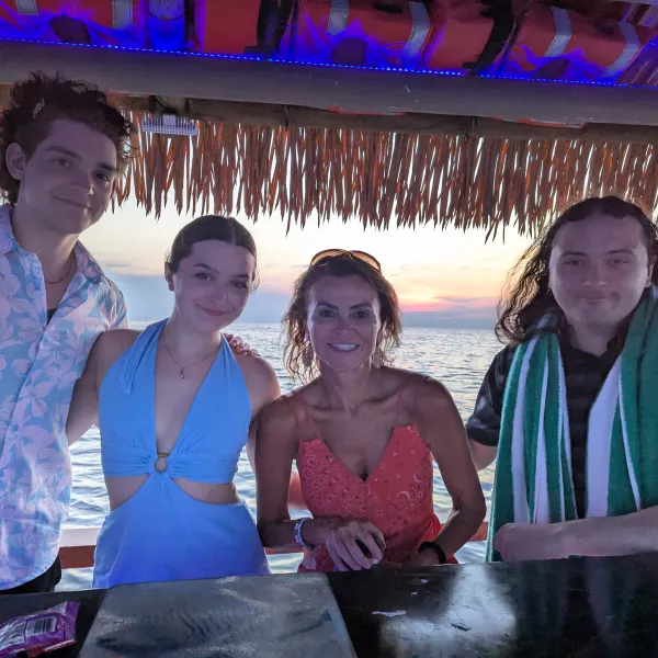 Four people smiling under a tiki hut with ocean sunset in background.