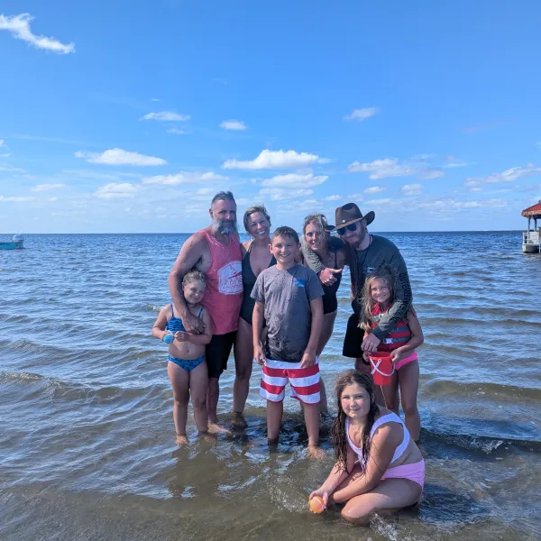 Group of people standing in shallow water at the beach under a blue sky.