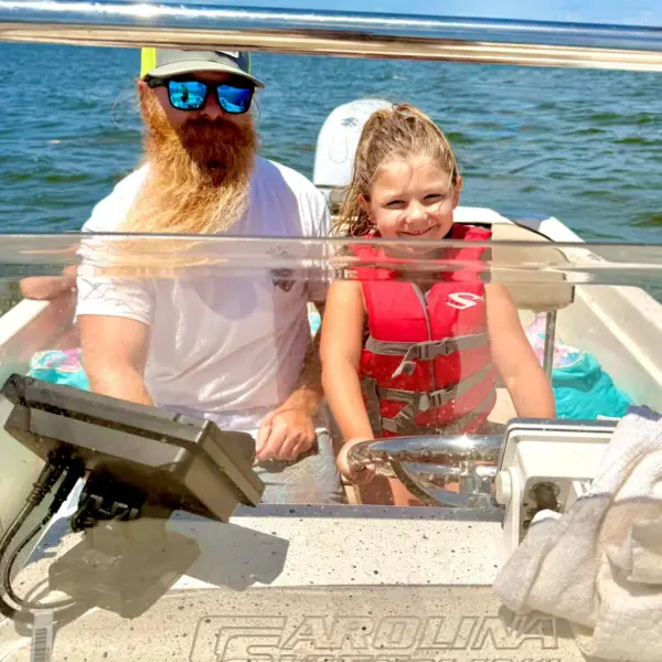 Man and child in life jacket on a boat in the ocean under a blue sky.