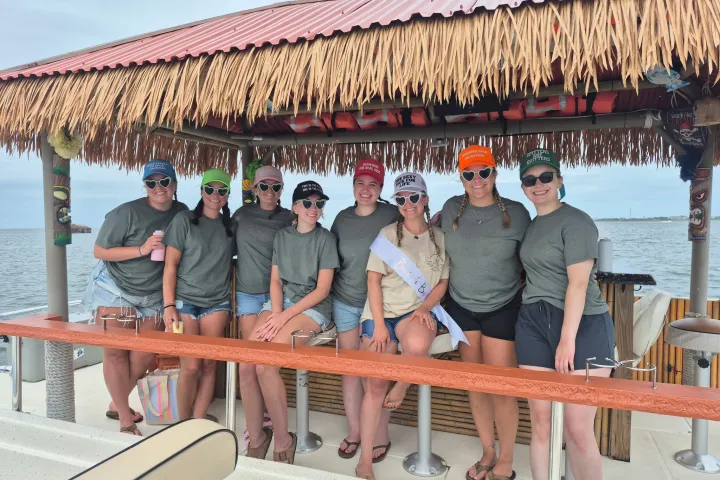 Group of women in matching outfits on a tiki boat smiling at the camera.