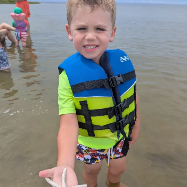 Child in life vest holding a starfish while standing in shallow water.