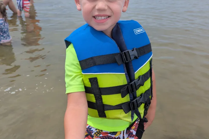 Child in life vest holding a starfish while standing in shallow water.