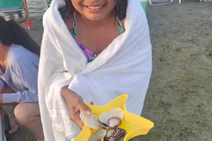 Child holding seashells in star-shaped container by the beach.