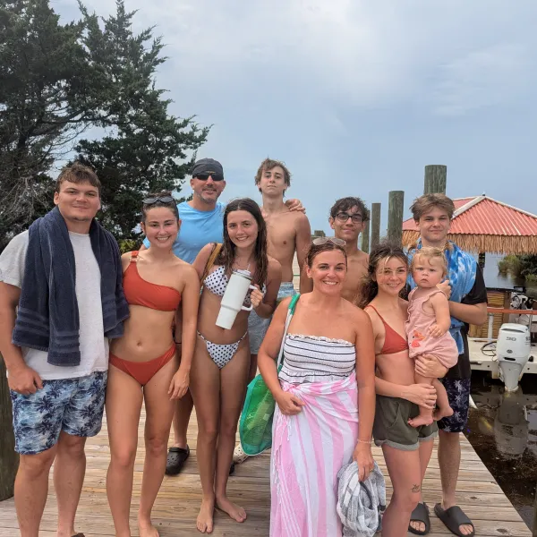 Group of people in swimwear standing on a dock by a small boat.