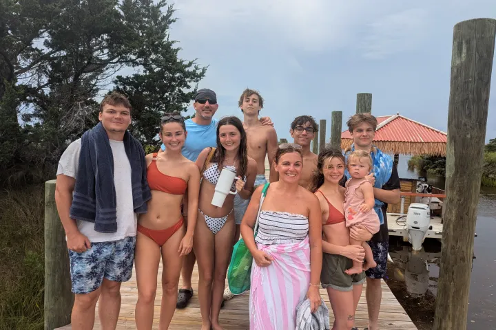 Group of people in swimwear standing on a dock by a small boat.