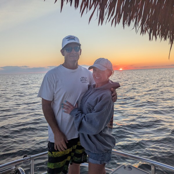 Couple on a boat at sunset with ocean in the background and thatched roof above.