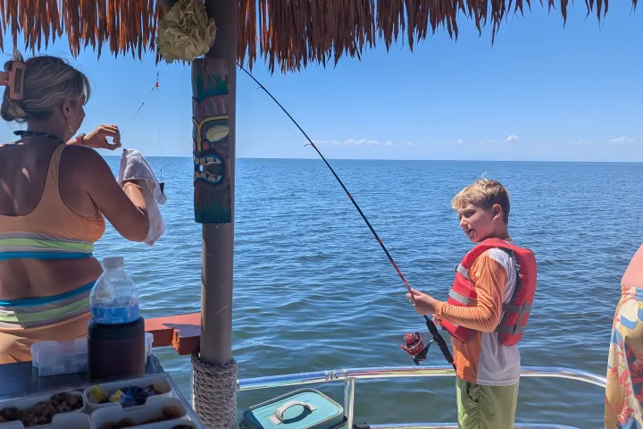Boy fishing on a boat under a thatched roof in sunny weather.