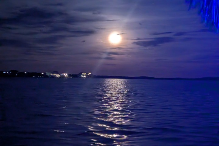 Moonlit night sky over a calm sea with clouds and reflections.