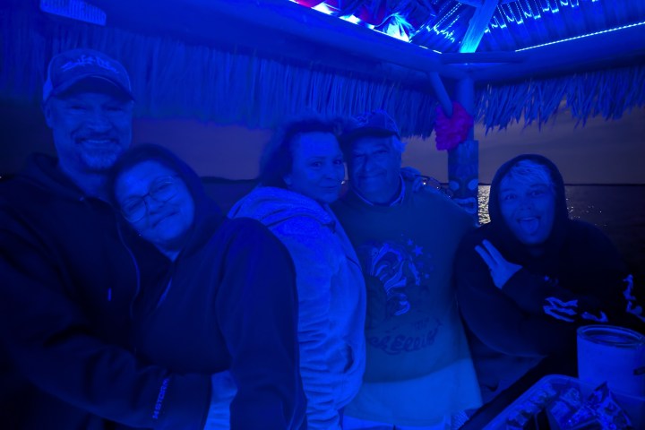 Group of people smiling under blue lighting on a boat at night.